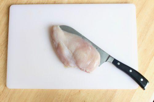 slicing the chicken breast in half ahead of marinading on a white cutting board