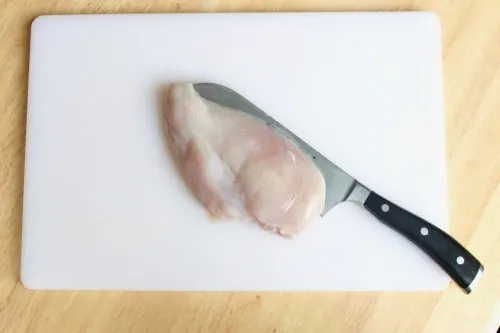 slicing the chicken breast in half ahead of marinading on a white cutting board