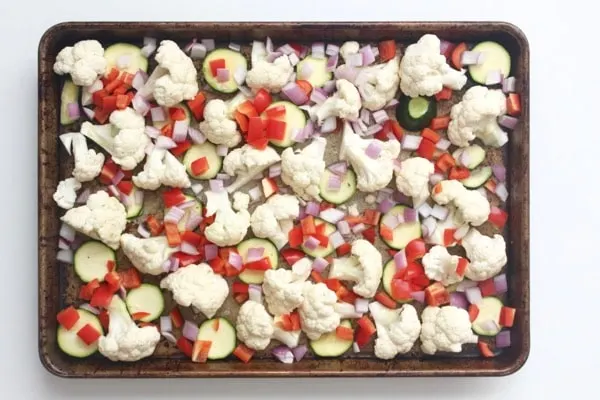 cauliflower, zucchini, red pepper and red onion on a roasting sheet