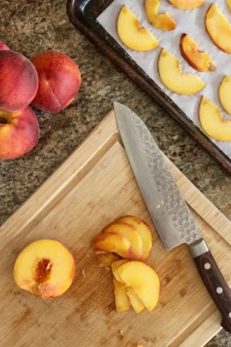 thinly slice peaches on a wooden cutting board and arranged on a parchment lined baking sheet