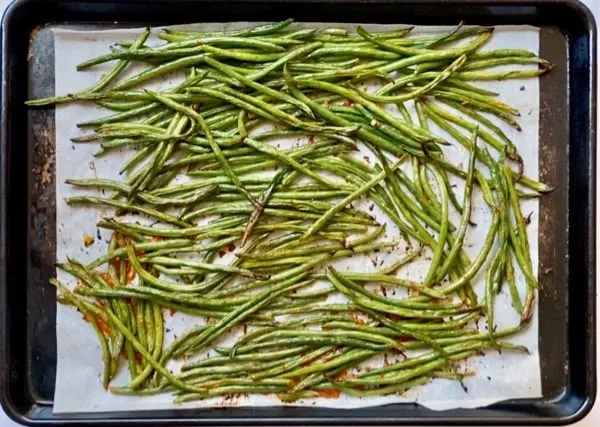 roasted harissa green beans on a parchment lined baking sheet