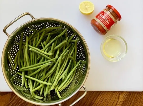 green beans in a metal colander with harissa, lemon and avocado oil