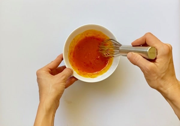 whisking together the harissa sauce in a white bowl