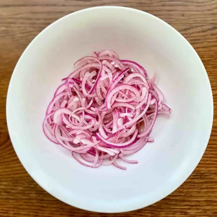 Quick pickled thinly sliced red onions in a white salad bowl
