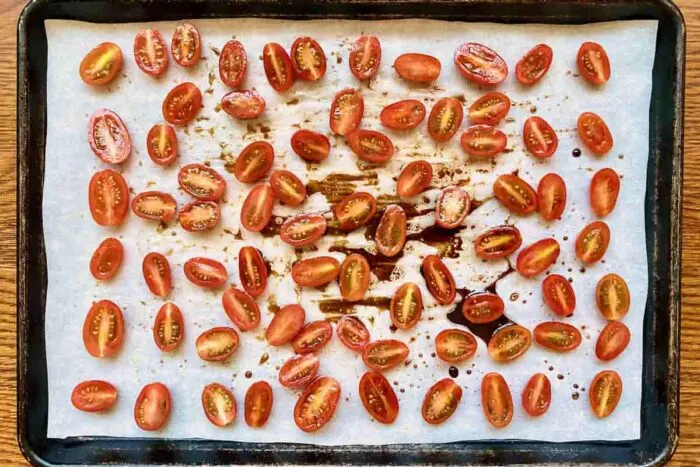 Cherry tomatoes tossed in balsamic vinegar and olive oil on a parchment lined baking sheet